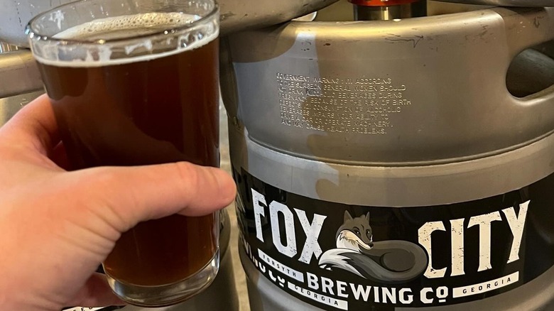 hand holding beer next to keg that says Fox City Brewing