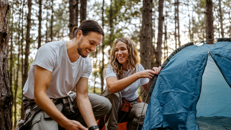 Two happy campers pitch a tent in the woods.