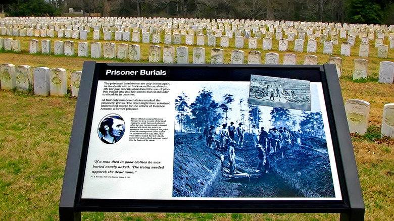 Educational sign about prisoner burials with gravestones behind it