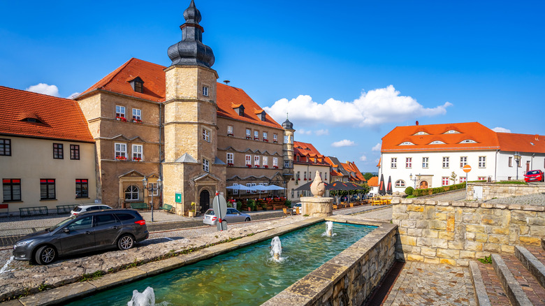The stone-walled town hall of Mücheln has a tower and fountain out front on a sunny day in Germany