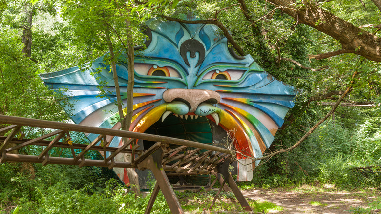 Rusty rollercoaster rails and a colorful tiger-face tunnel entrance in an abandoned amusement park