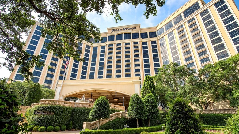 Upward exterior image of Beau Rivage Resort and Casino during the day with trees in the foreground.