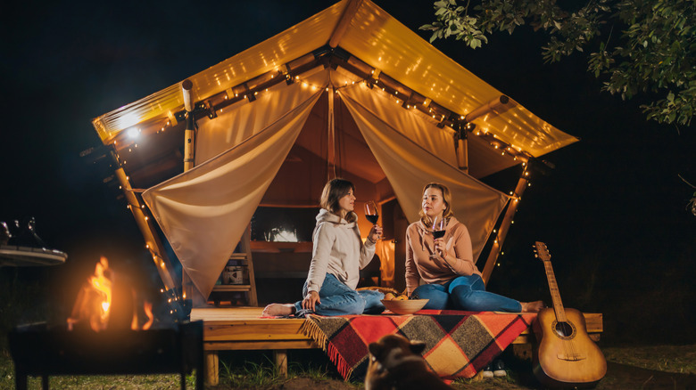 Two people sitting in cozy glamping tent in autumn evening bonfire