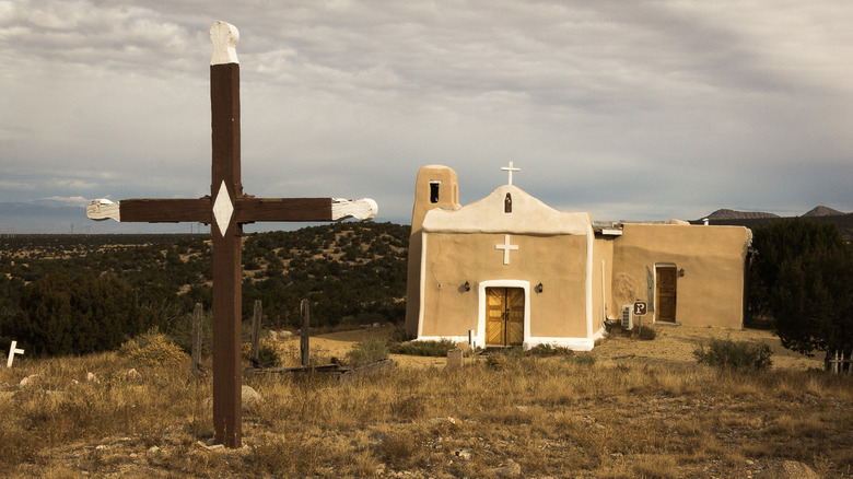 The San Francisco de Asis Catholic Church from a distance with a brown and white cross in the foreground.