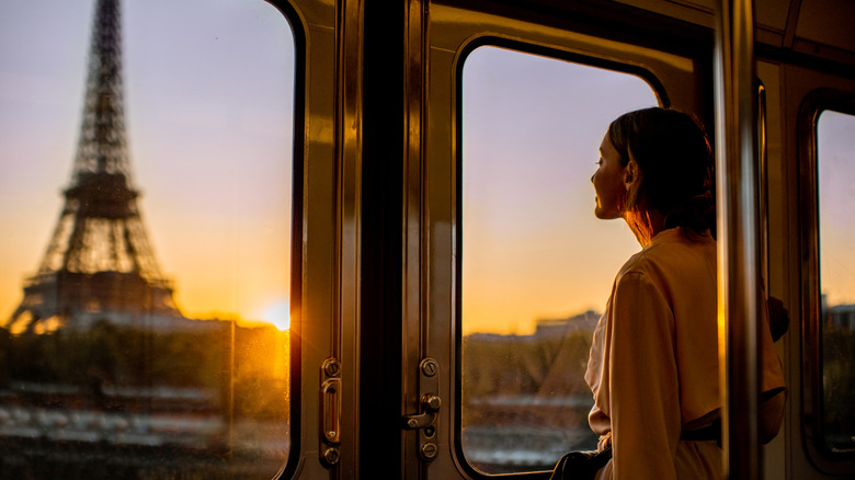 A young woman enjoys a view of the Eiffel Tower in Paris, France at sunrise from the window of a train that passes by this landmark