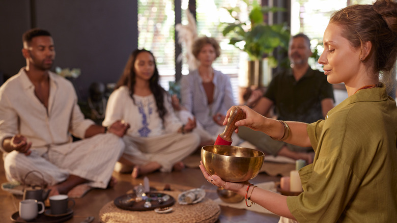 A female guru with a singing bowl with a group of participants in meditating positions
