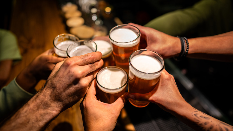 Close-up image featuring the hands of several people holding pints of beer and cheering over a bar counter