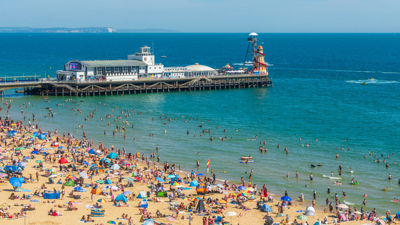 Clear waters and sandy beaches crowded with umbrellas with pier building in background in Bournemouth, England