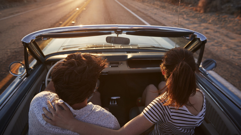 Straight couple from behind driving convertible on open road