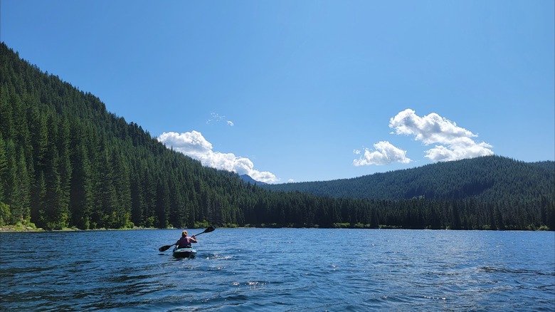 A paddler on Walupt Lake, Washington, with tree-clad mountains surrounding the water under a blue sky