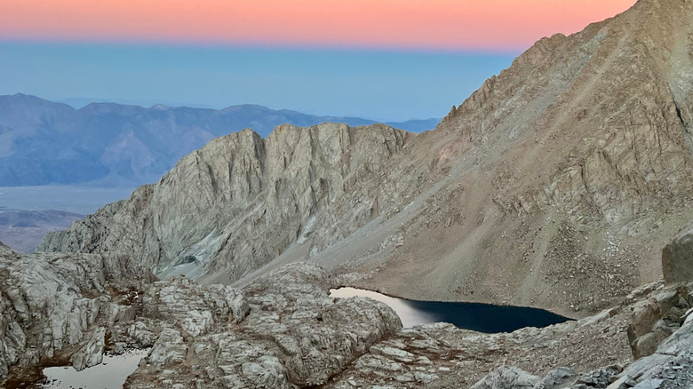 Stark greyish granite mountains surrounding Consultation Lake with a pink and blue sky above and mountains in the background