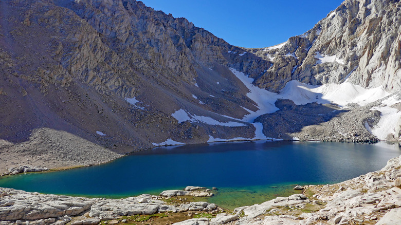 Afternoon view of Consultation Lake along the Mt. Whitney Trail, snow on the hillsides and granite peaks surrounding the water