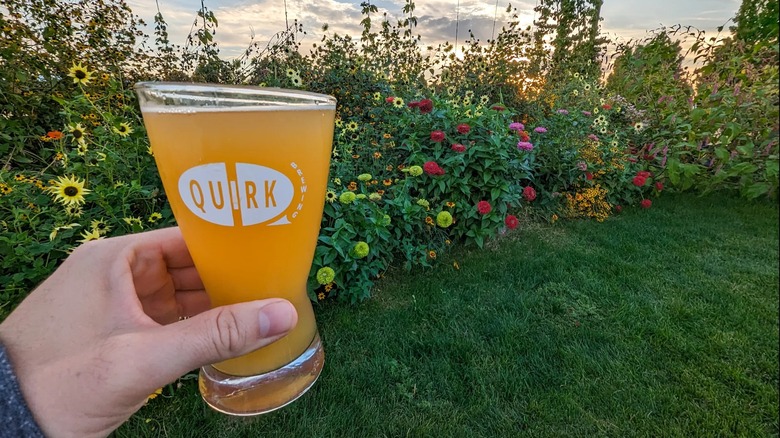 A hand holding a draft beer in front of flower beds outdoors at Quirk Brewing in Walla Walla County, Washington