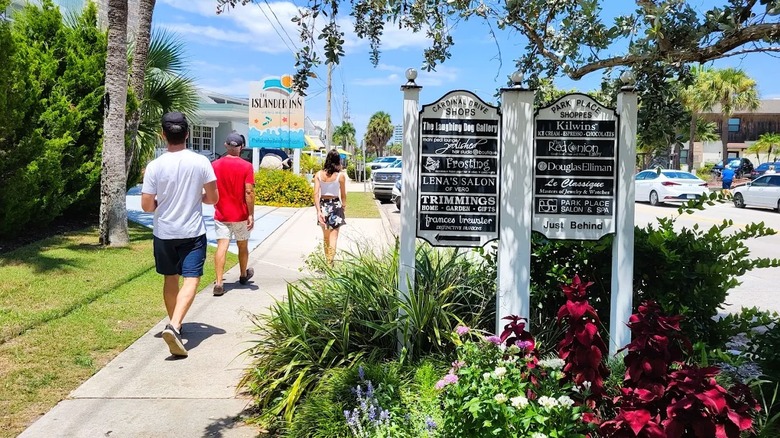 Pedestrians walking past flowers, trees, and shop signs in Vero Beach, Florida