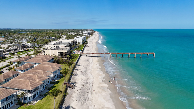 An aerial view of the Atlantic, a pier, and Vero Beach's white sand lined with palm trees and condos