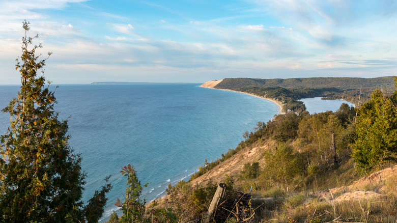 Scenic overlook on the Empire Bluffs Trail overlooks Lake Michigan, Sleeping Bear Dunes National Lakeshore, South Manitou Island, and North Bar Lake, under a blue sky with white clouds.