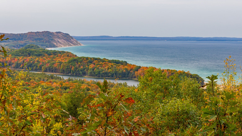 View of distant Empire Bluff sand dunes along shore of Lake Michigan with North Bar Lake in foreground surrounded by brilliant fall foliage