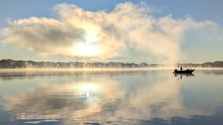 Angler on a boat on Reeds Lake, Michigan, with calm waters reflecting the cloudy sky
