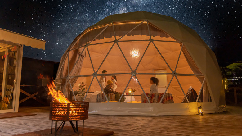 A family inside a geodesic dome under starry skies with a firepit in the foreground