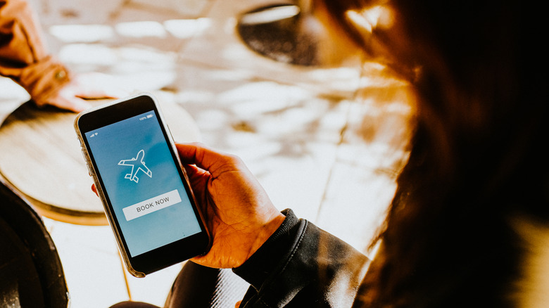 Hand holding a phone with a generic "book now" text and image of an airplane