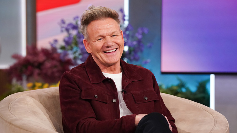 Chef Gordon Ramsey smiles while sitting on a couch during an interview