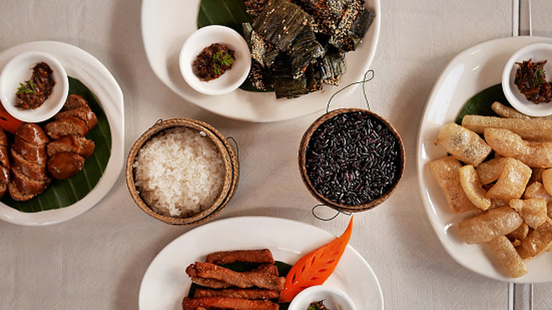 A top view shot of four plates of fried meat dishes with condiments and a bowls of white and black rice