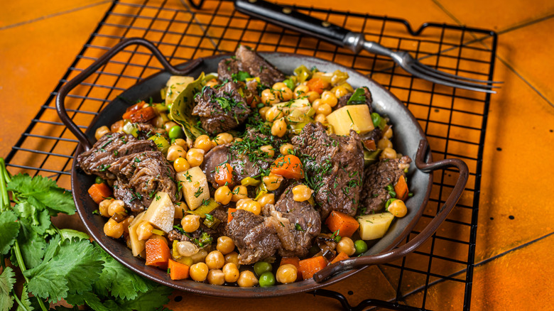 A plate of beef, chickpeas, carrots, and potatoes with herbs and a fork in the background