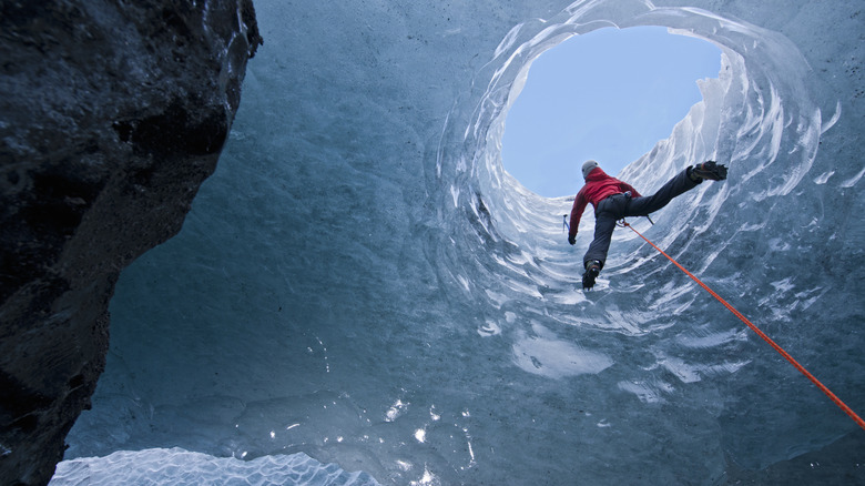 Person climbing through ice wall in a glacier cave