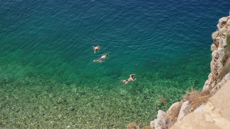 View from the cliff of the beautiful clear water of Hydra, Greece, with several swimmers