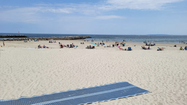 A view of Green Harbor beach and people resting on the sand with a stone jetty in the background