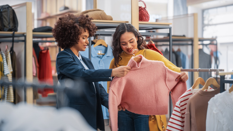 Two women shoppers examining a pink sweater at a boutique.