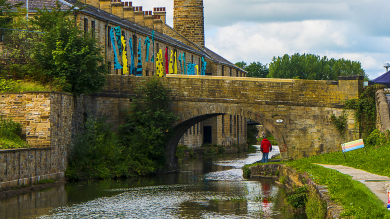 A view of the canal in Burnley, UK, with water running beneath an old stone bridge and banked by a stone building.