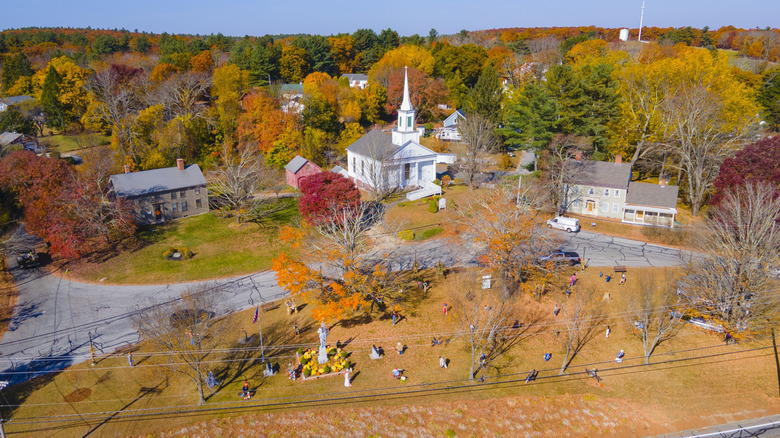 An aerial view of Douglas, Massachusetts, a village with a cemetery and white steepled church, in autumn