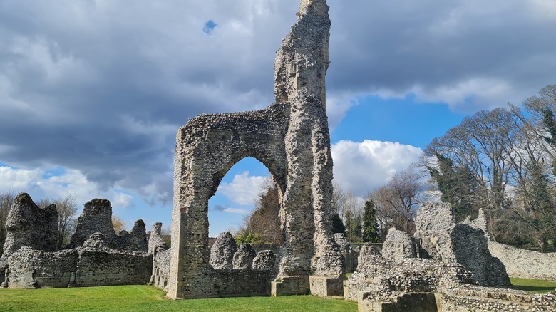 Stone ruins of Thetford Priory with cloudy skies on a grass field