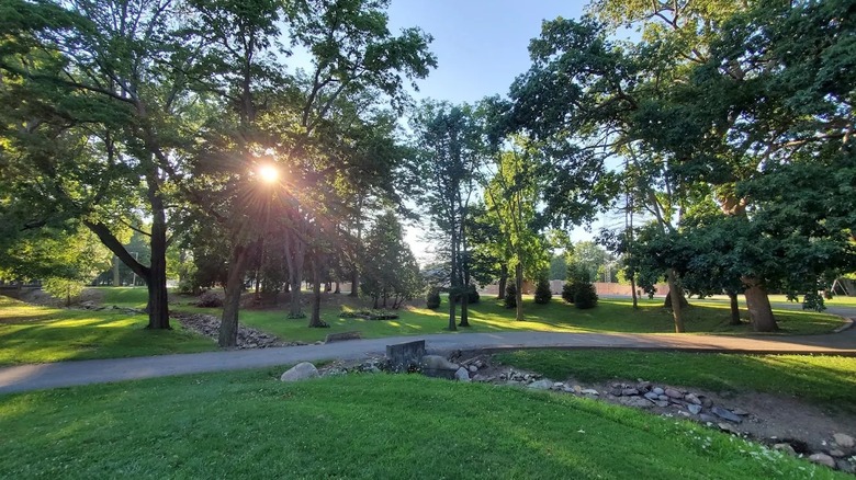 Matter Park in Indiana, featuring lush grass with paved trails, stone features, and the sun shining between the trees.