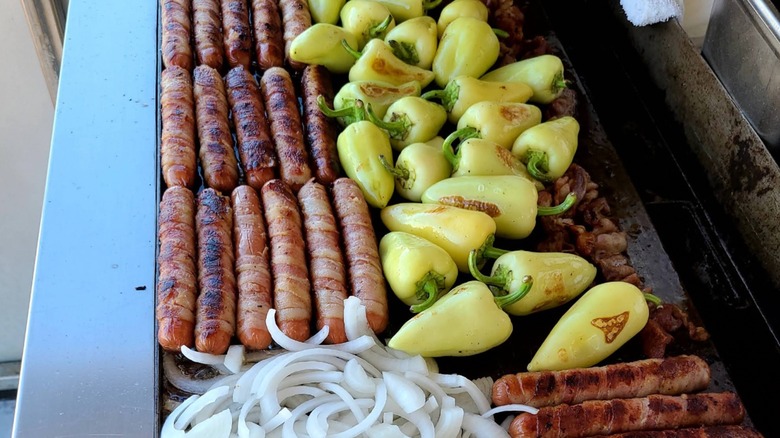 Rows of bacon-wrapped hot dogs, peppers, and onions on grill Chino's Tucson