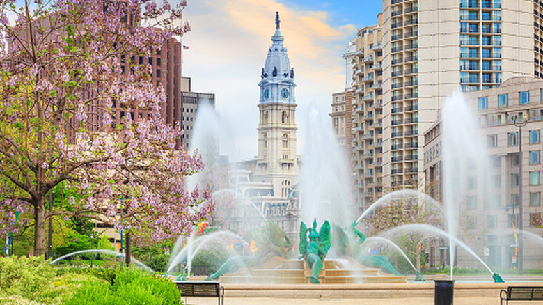 Geysers of water arc over a fountain as City Hall's tower rises in the background on a sunny day in Philadelphia