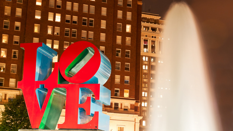 The LOVE sculpture stands next to a blasting fountain of water during a night scene in Philadelphia