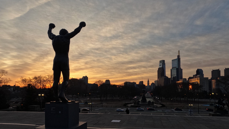 The Rocky Statue is silhouetted against a cloudy sky as Philadelphia's skyline frames a sunset
