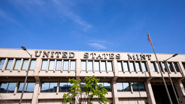 A sign for the United States Mint hangs on top of a building made of concrete and glass on a sunny day in Philadelphia