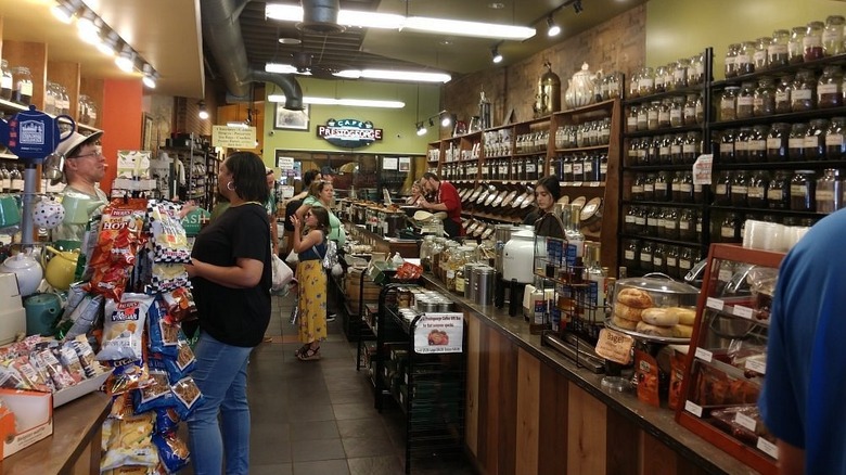 Interior of Prestogeorge, with teas and coffees along the right wall, a sign on a yellow back wall, a wood counter, and patrons shopping