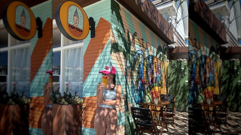 Woman sipping on a drink beside the mural outside Fish Company Taco