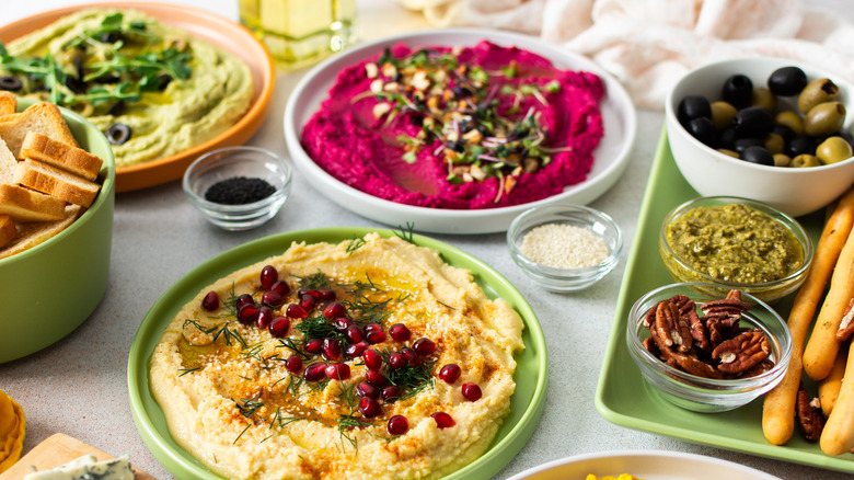 A vibrant vegan feast of hummus, beetroot hummus, olives, nuts, toasts, and breadsticks.