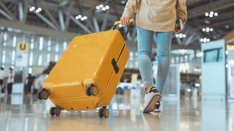 person wheels hard-sided luggage through airport
