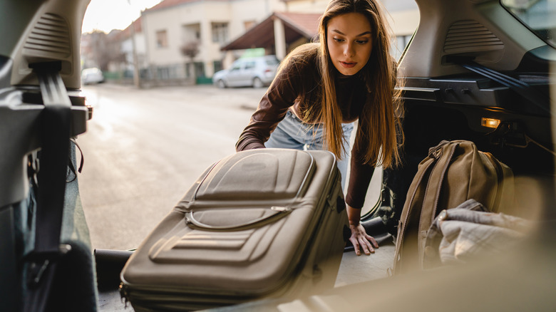woman puts soft-sided suitcase in car trunk