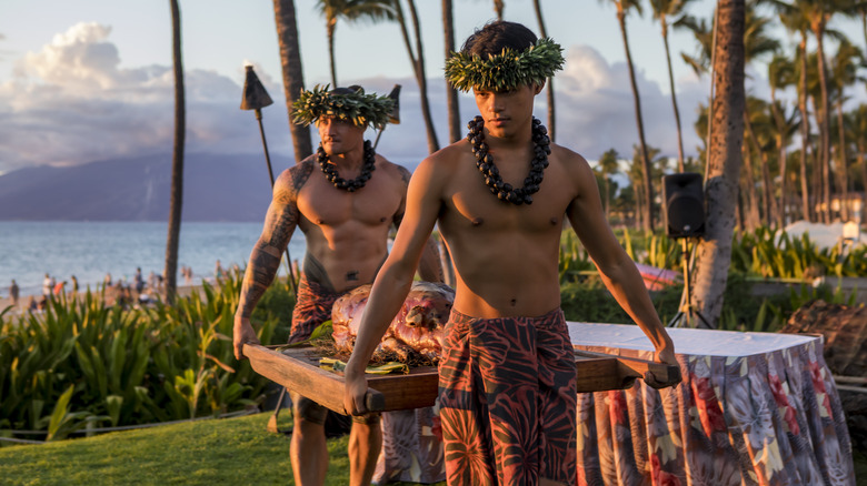 Luau entertainers in traditional dress on Maui carrying a pig to a roasting pit during the umu ceremony