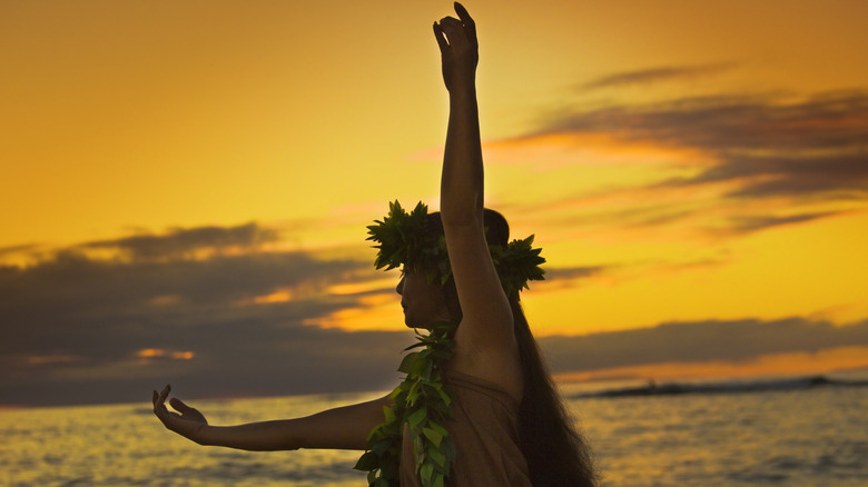 A beautiful Hawaiian hula dancer dancing on the beach silhouetted against the sunset