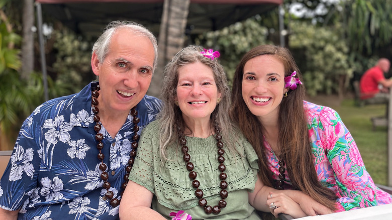 Senior couple poses with their adult daughter in upscale island attire at a Hawaiian luau