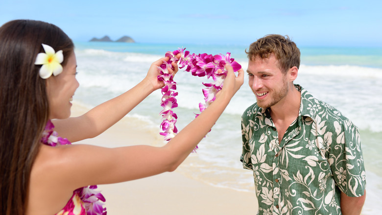Native Hawaiian woman offering a purple orchid lei greeting to a tourist