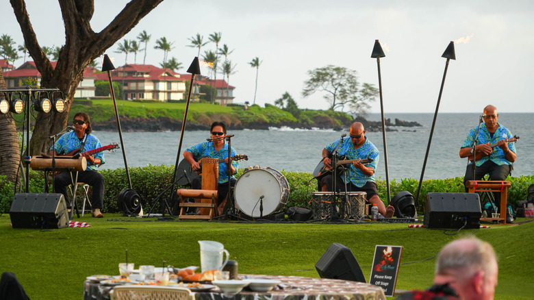 Polynesian music band playing the ukulele and the guitar in front of the Pacific Ocean at the Te Au Moana Luau dinner-show